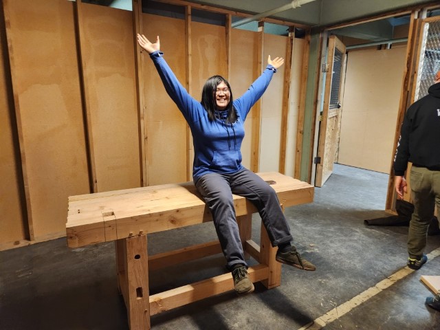 me, sitting on top of the assembled workbench. My arms are raised triumphantly, and I have a huge smile on my face.