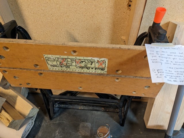 An old black-and-decker Workmate folding workbench with a note sticked on. It was generously given to me by someone in a neighboring unit to mine.
